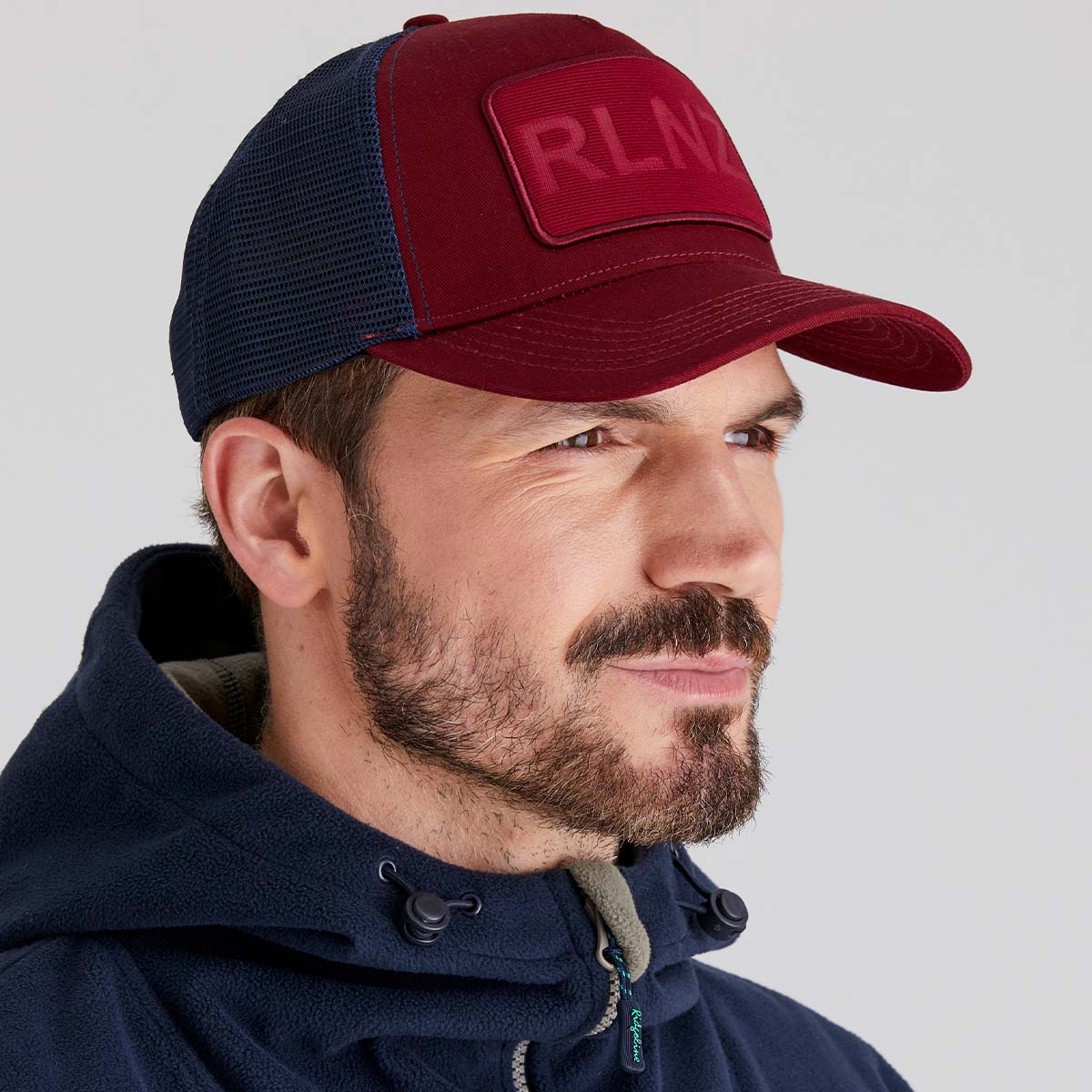 Man wearing a red and navy cap with 'RLNZ' logo on a light grey background