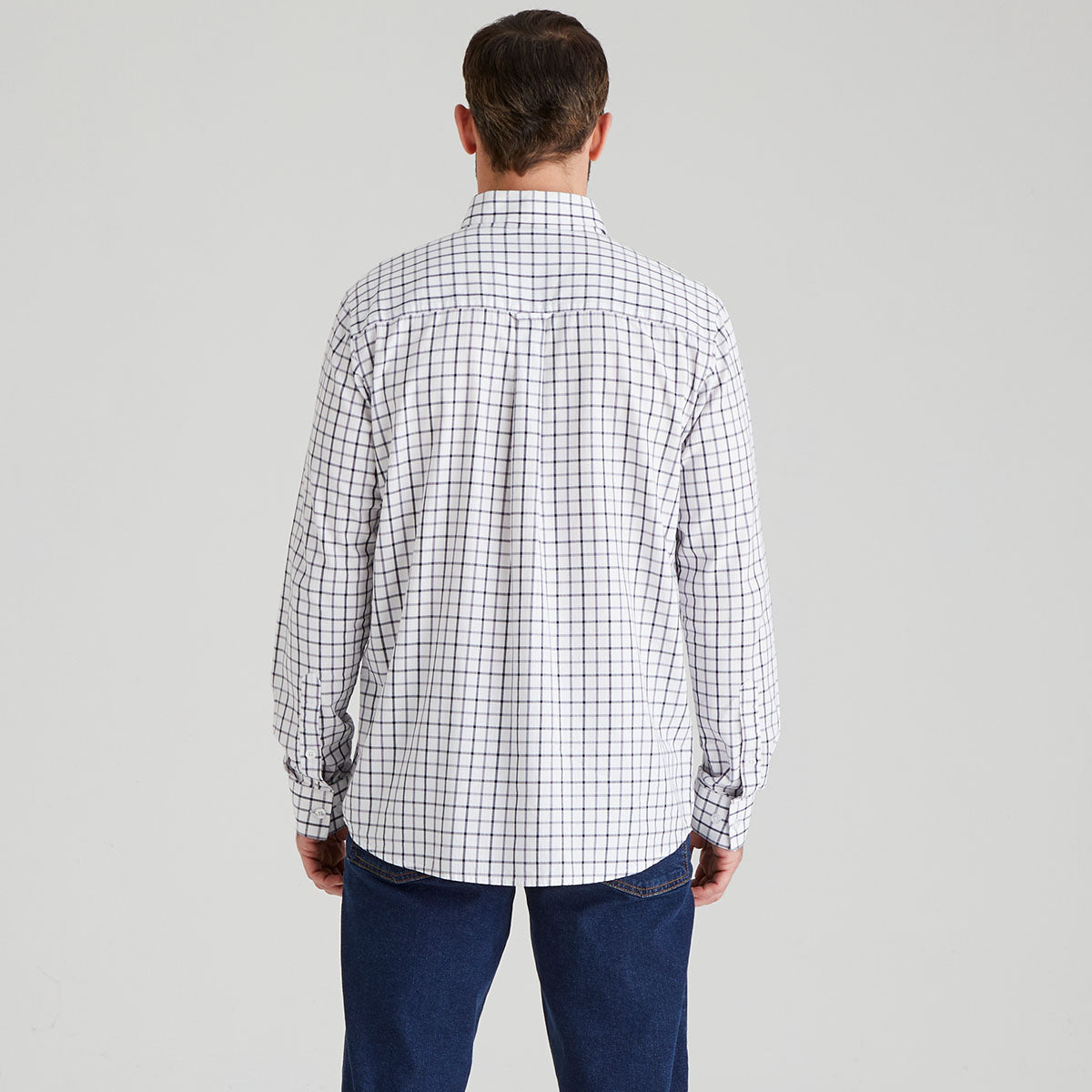 Man wearing a checkered shirt open and blue jeans on a grey background