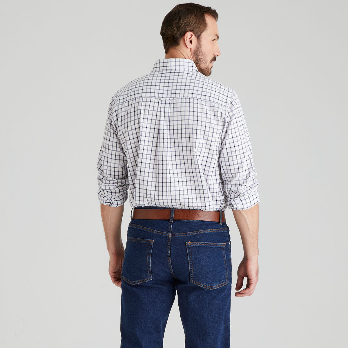 back of man wearing a checkered shirt tucked in and blue jeans on a grey background
