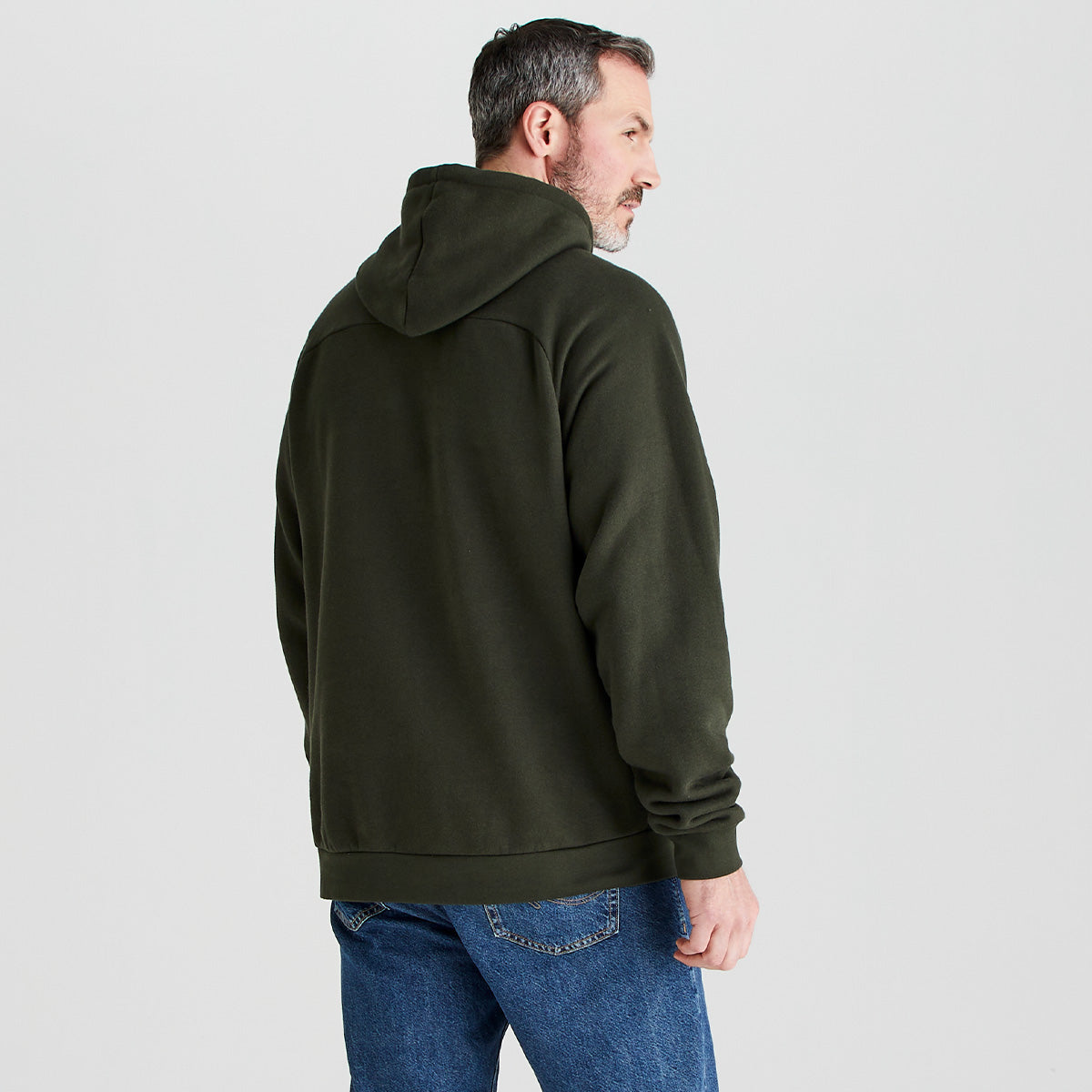 Man wearing a green hoodie and blue jeans on a light gray background