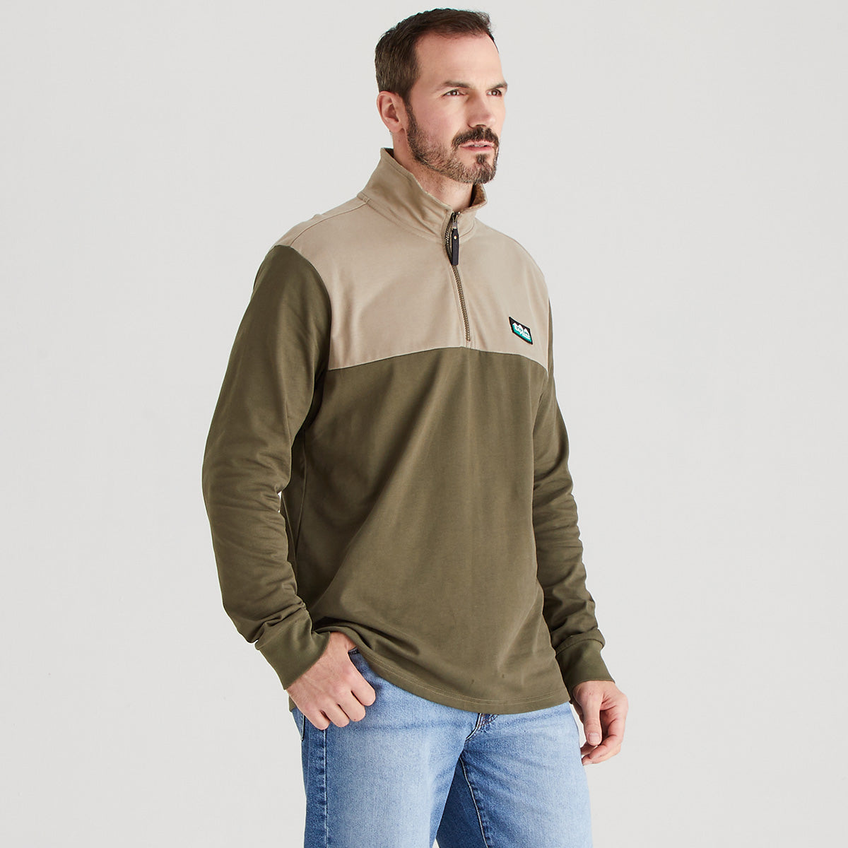 Man wearing a two-tone pullover with a visible brand logo on a light gray background