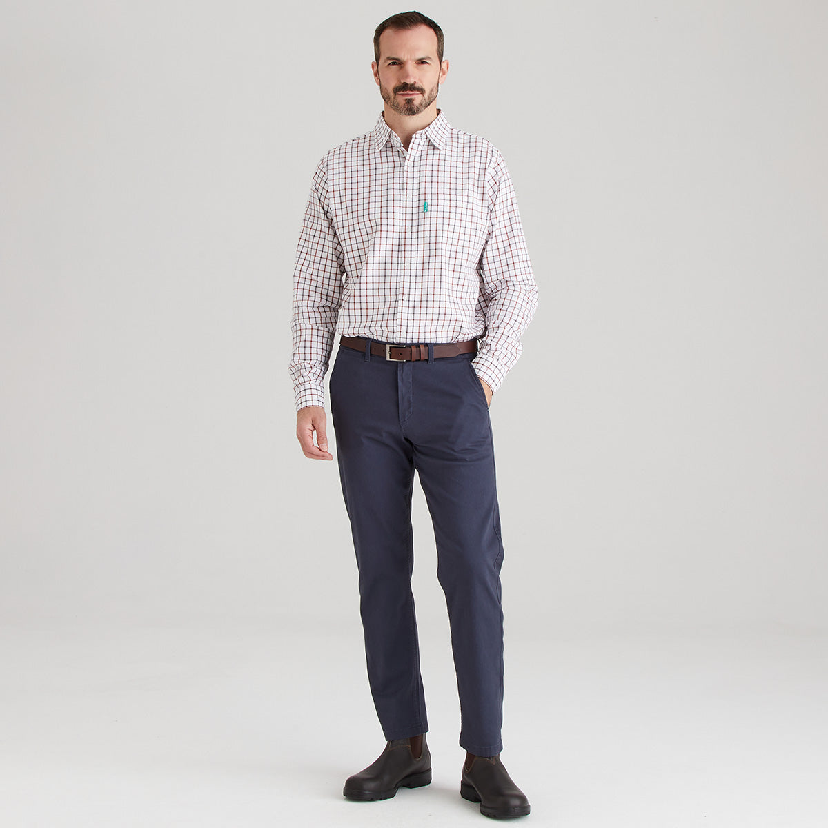 Man wearing a checkered shirt and navy pants on a light gray background