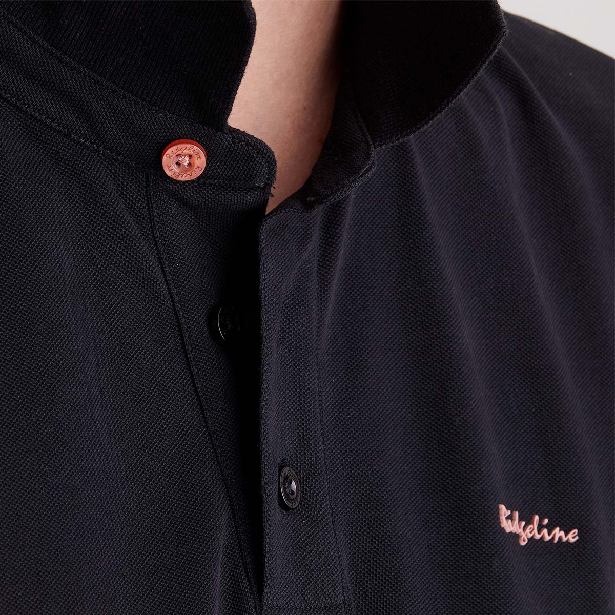 Close-up of a black polo shirt with a brand logo on a neutral background
