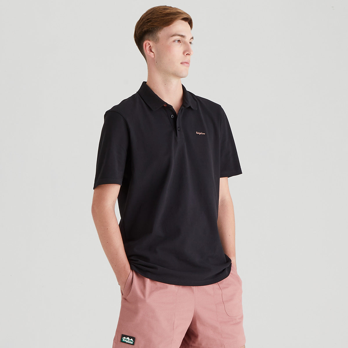 Man wearing a black polo shirt with a brand logo on a light gray background