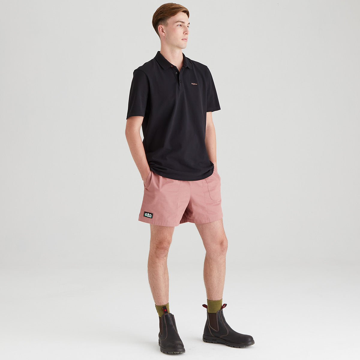 Man wearing a black polo shirt and pink shorts on a white background