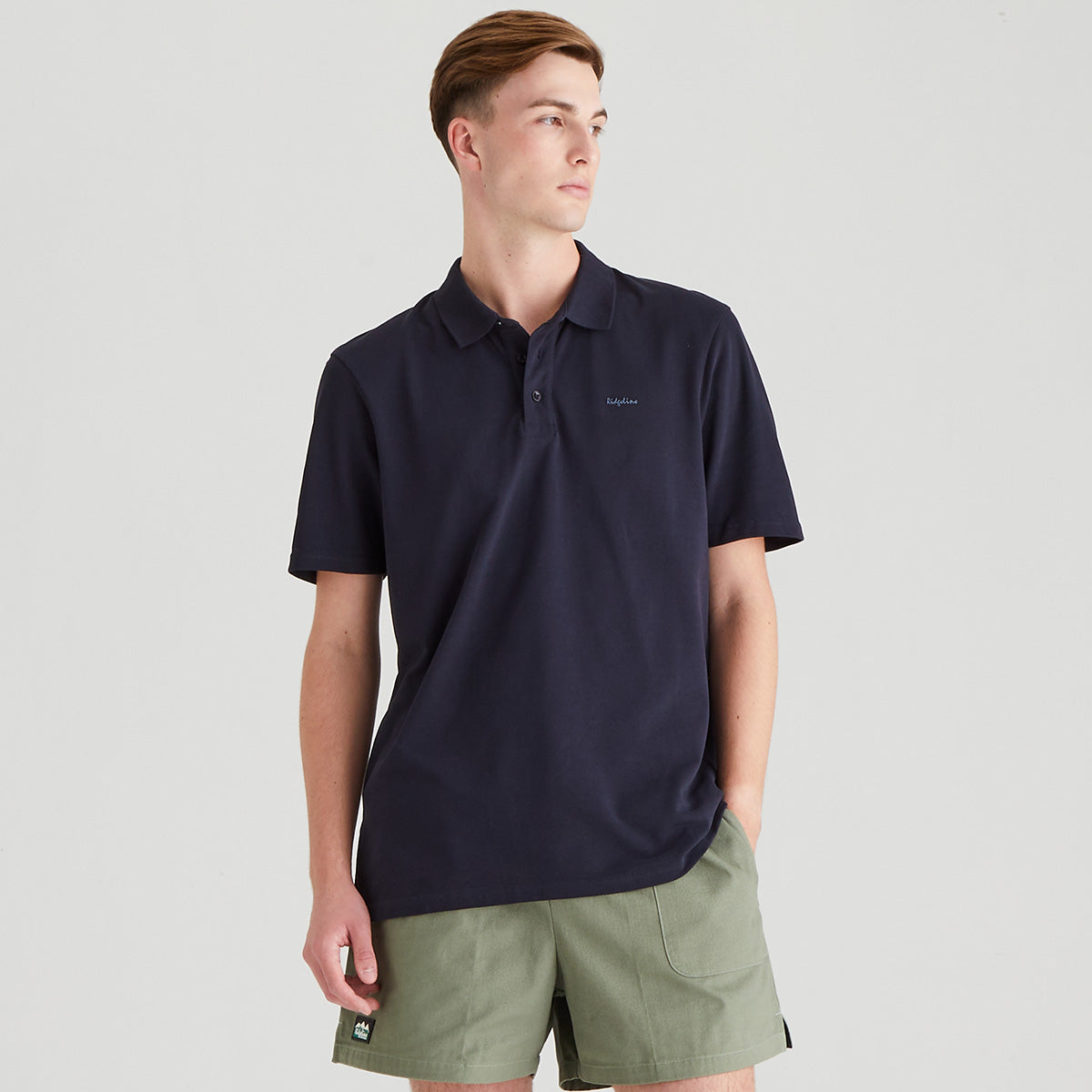Man wearing a navy polo shirt and green shorts on a light gray background