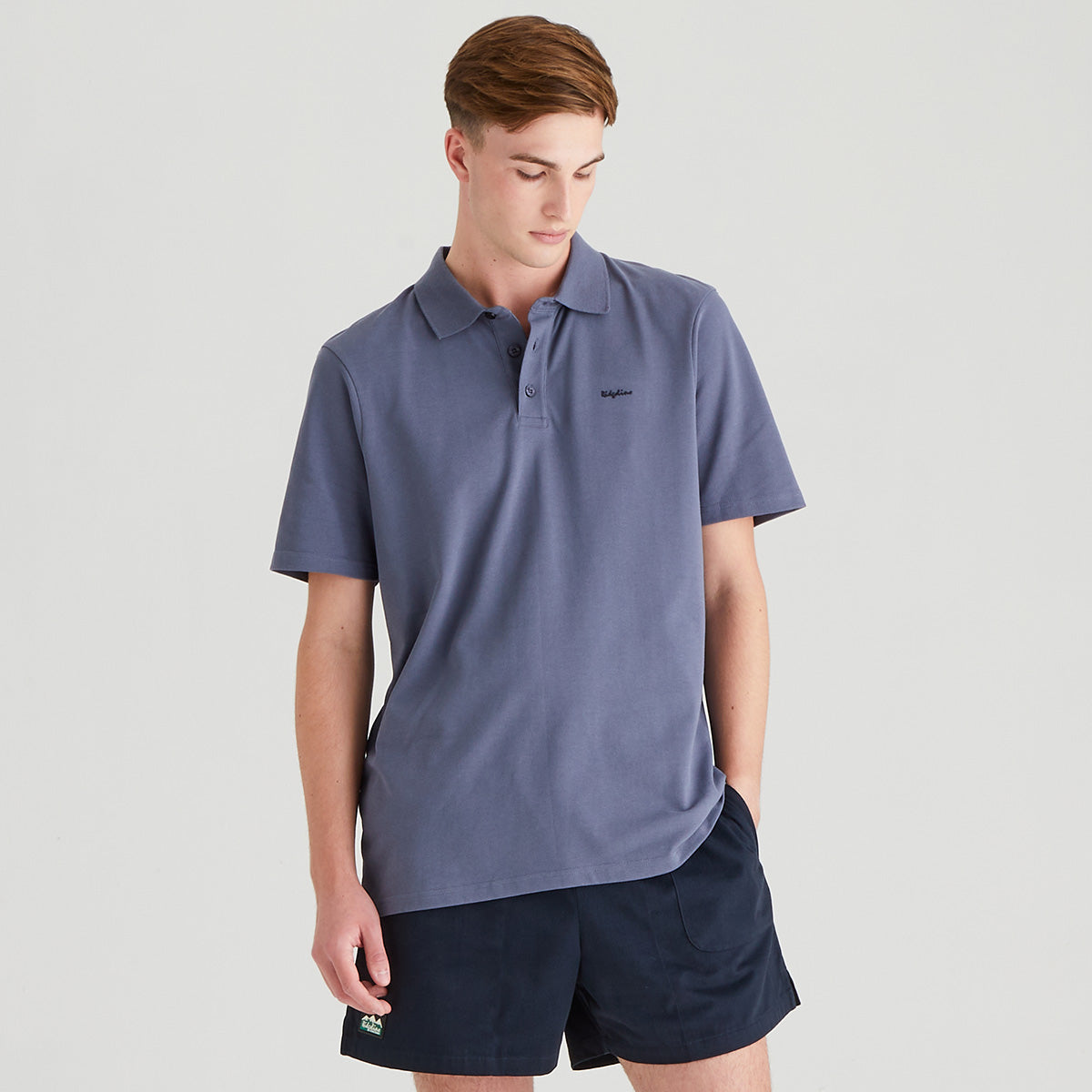 Man wearing a blue polo shirt and navy shorts on a light gray background