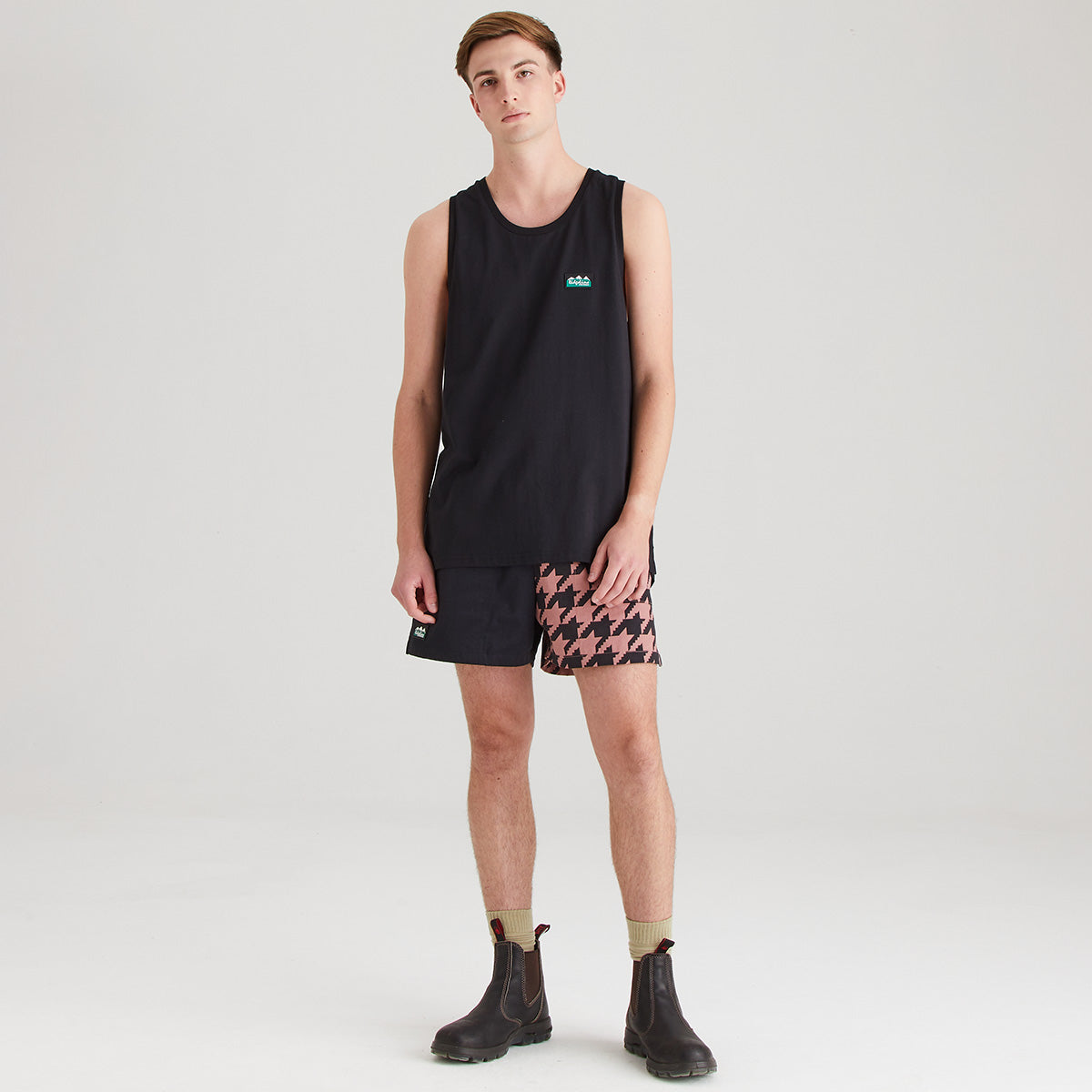 Person wearing a black sleeveless shirt and patterned shorts on a white background