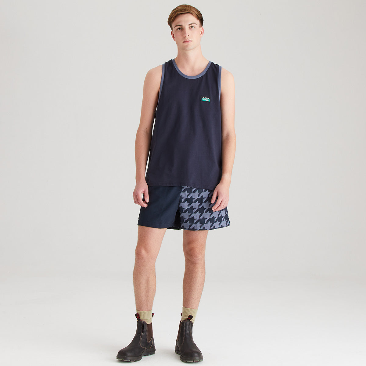 Person wearing a navy tank top and patterned shorts on a light gray background