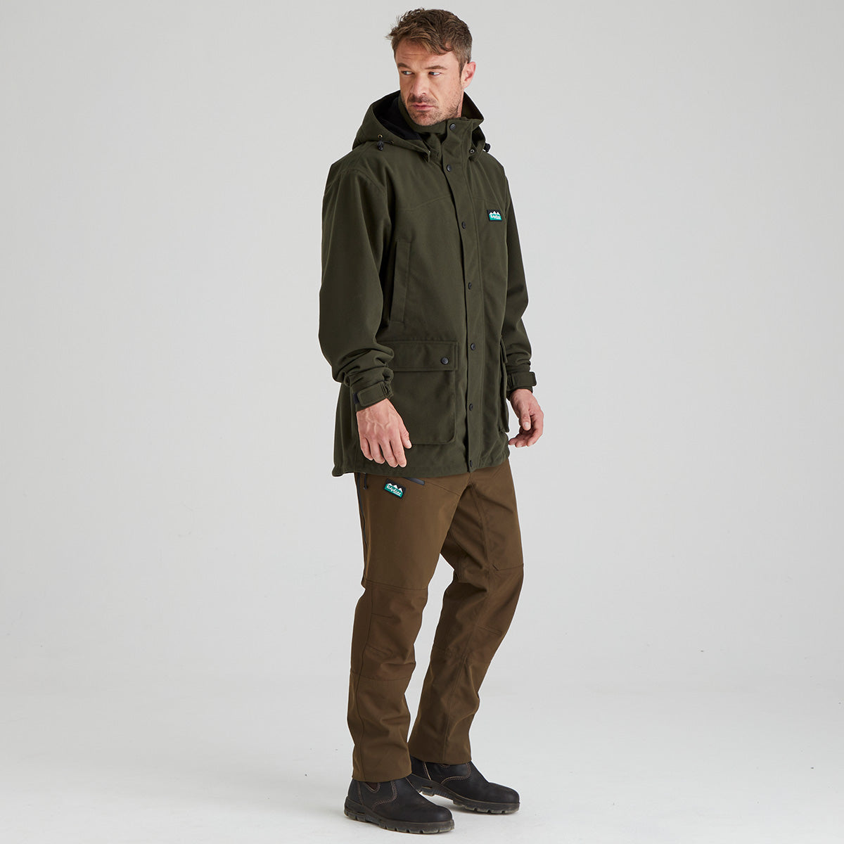 Man wearing a green jacket and brown pants on a white background
