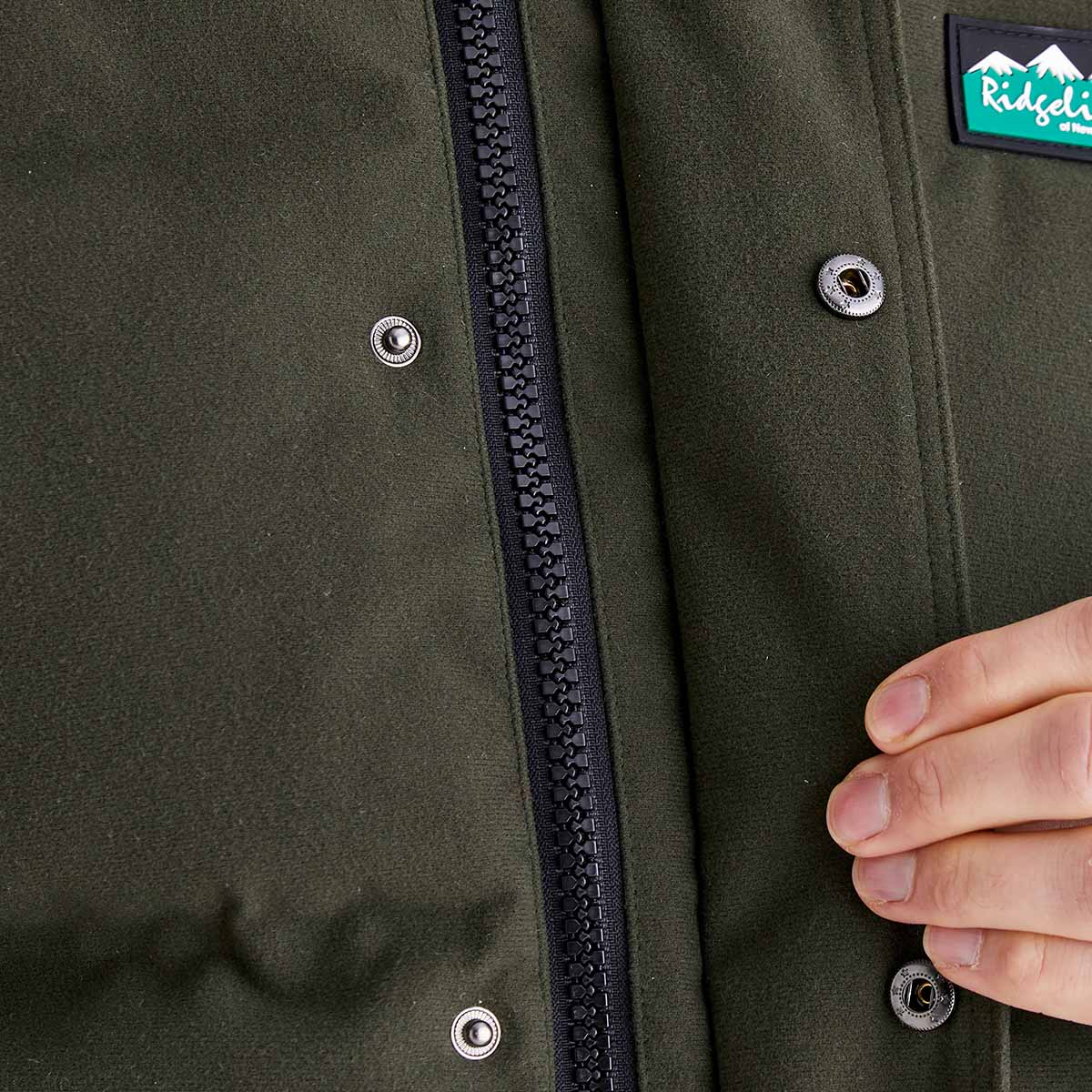 Close-up of a green jacket with a zipper and buttons, featuring a brand patch.
