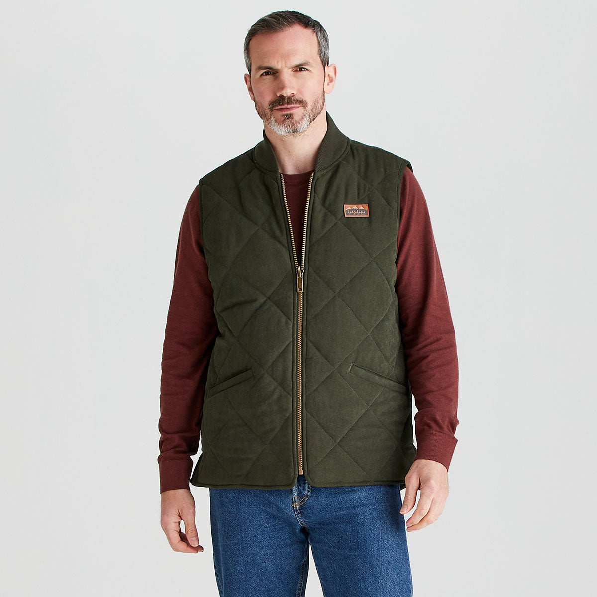 Man wearing a green quilted vest over a red long-sleeve shirt on a white background