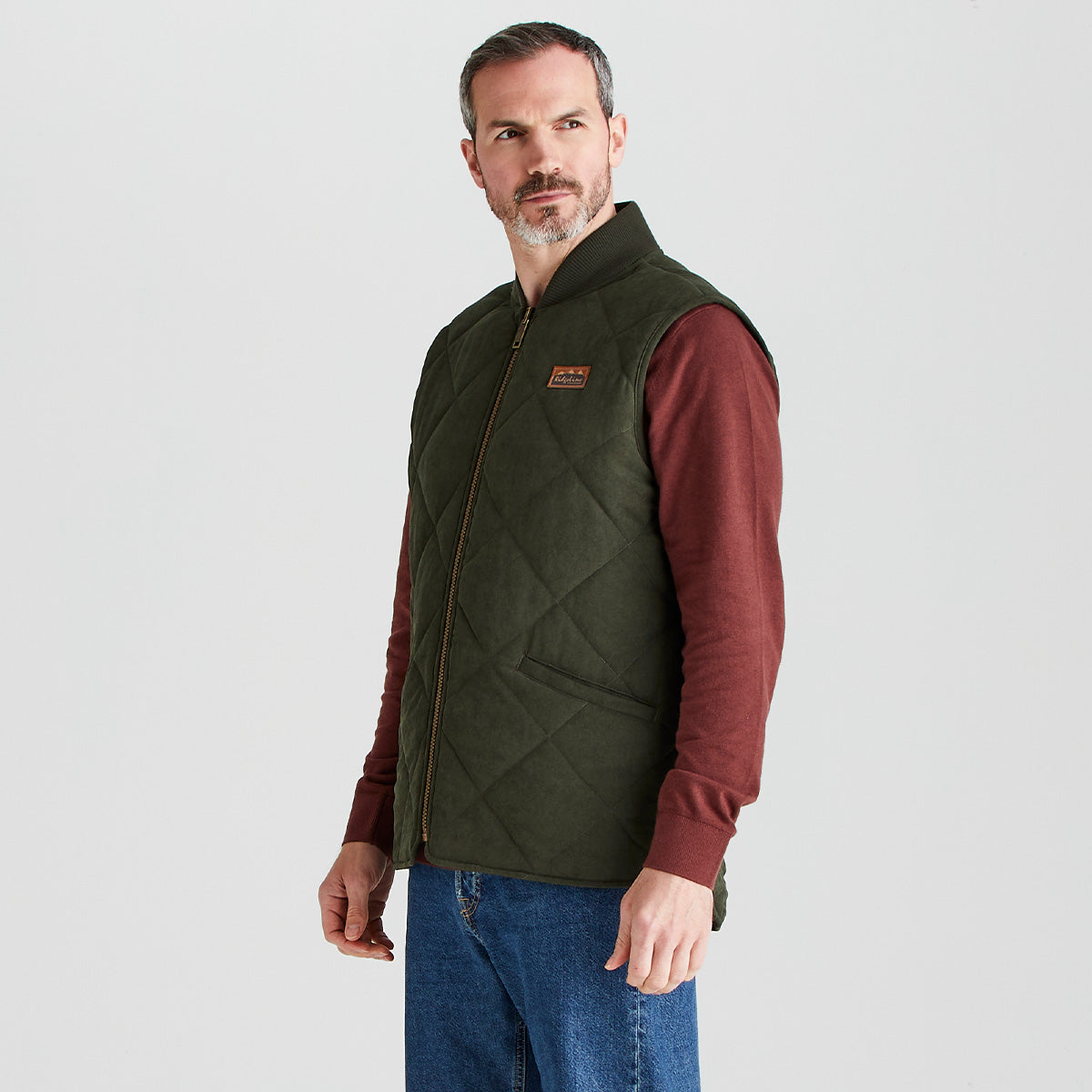 Man wearing a green quilted vest over a red shirt on a light gray background