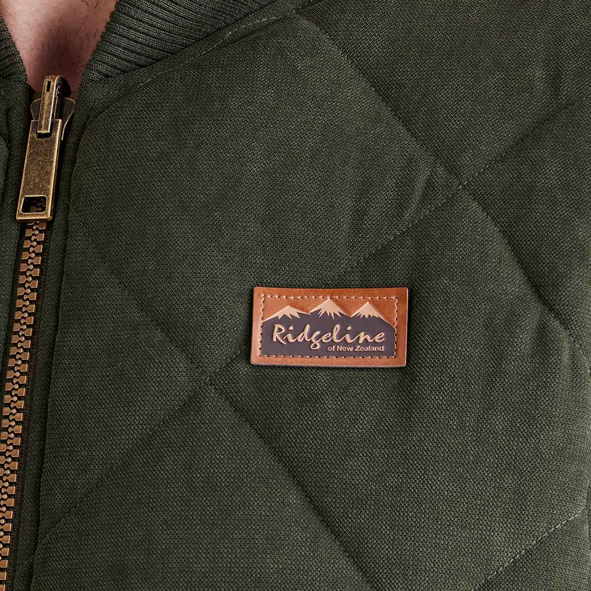 Close-up of a green quilted jacket with a leather patch on a person wearing it.