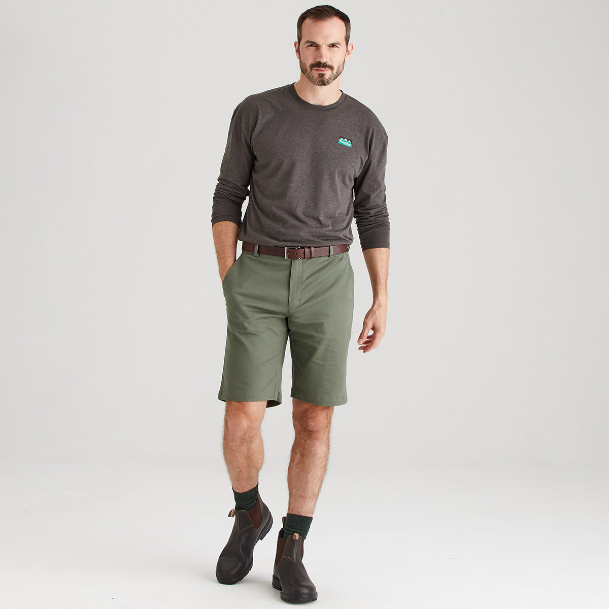 Man wearing a gray long-sleeve shirt and green shorts on a white background