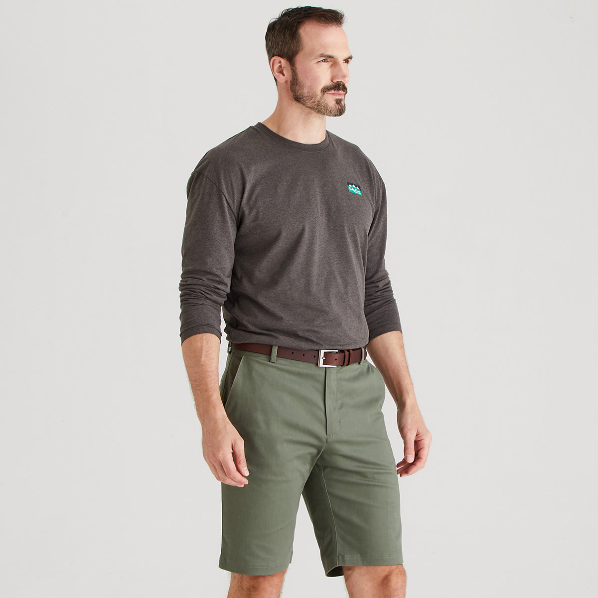 Man wearing a gray sweatshirt with a logo and green shorts on a light gray background