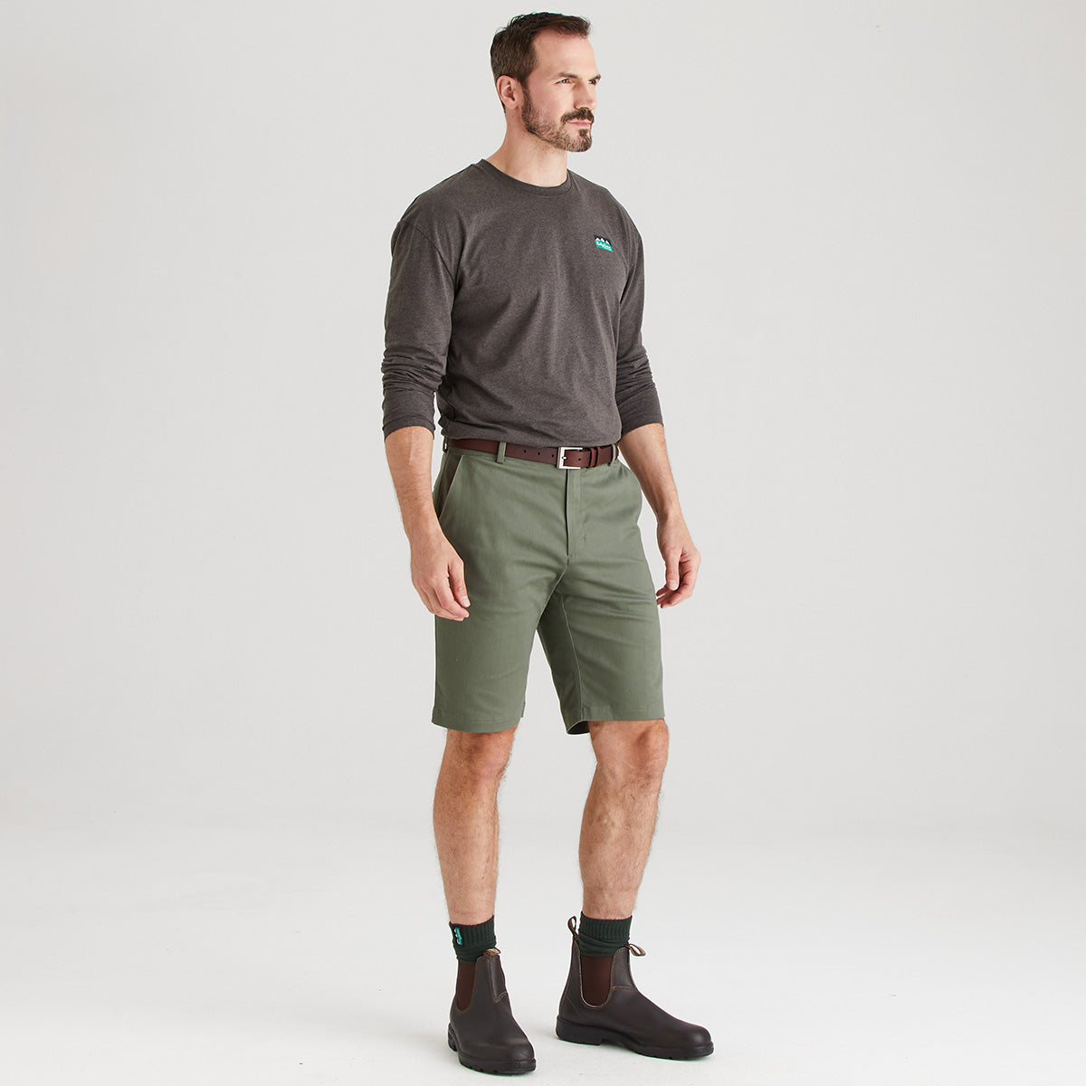 Man wearing a gray long-sleeve shirt and green shorts on a white background