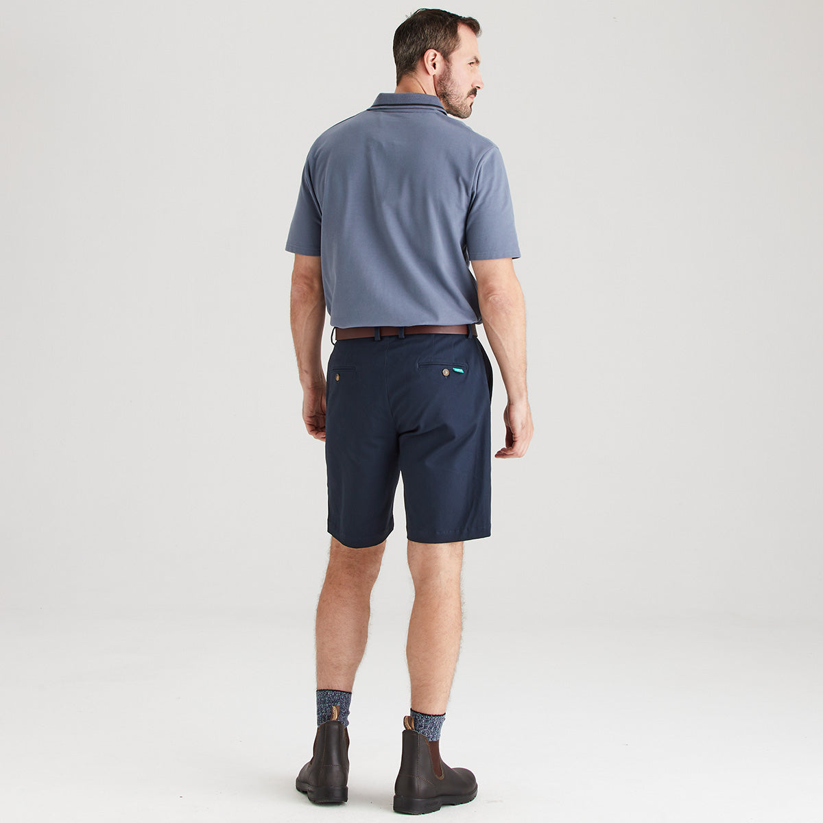 Man wearing a blue polo shirt and navy shorts on a white background