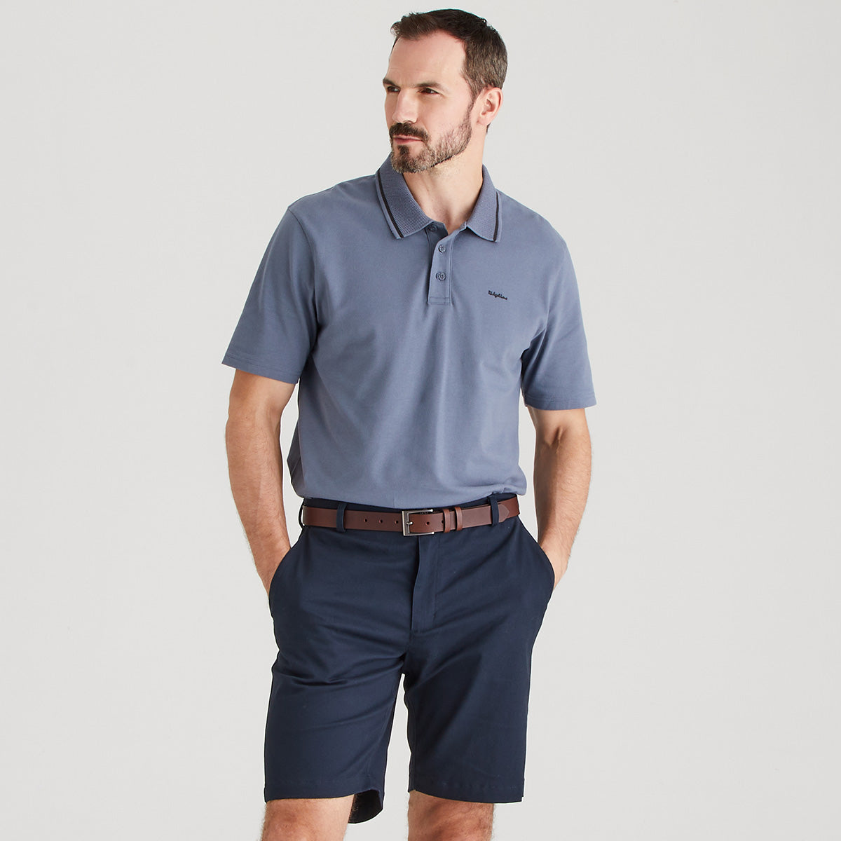 Man wearing a gray polo shirt and navy shorts on a light gray background