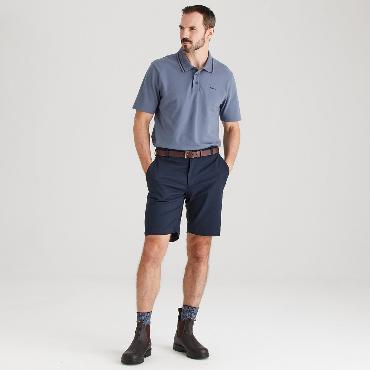 Man wearing a gray polo shirt and navy shorts on a white background