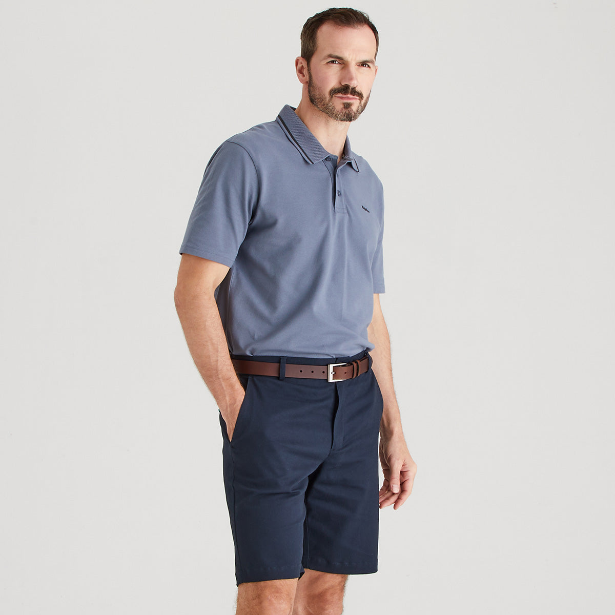 Man wearing a blue polo shirt and navy shorts on a light gray background