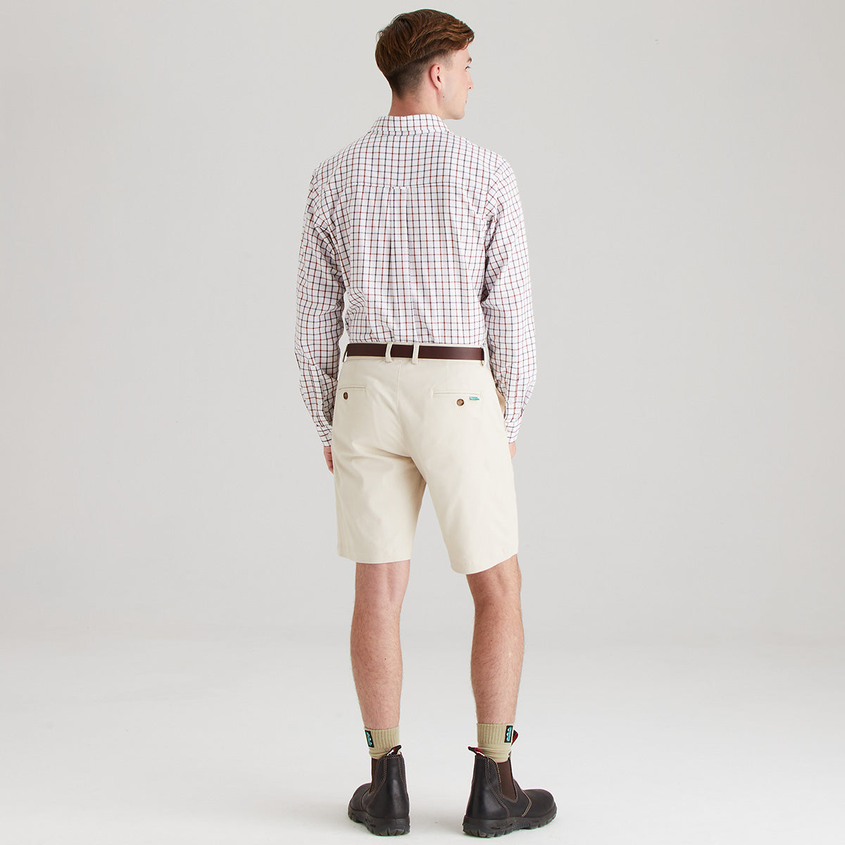 Man wearing a checkered shirt and beige shorts on a plain background