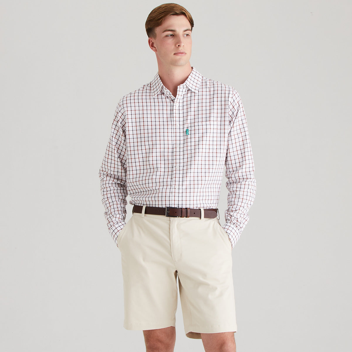 Man wearing a checkered shirt and beige shorts on a gray background