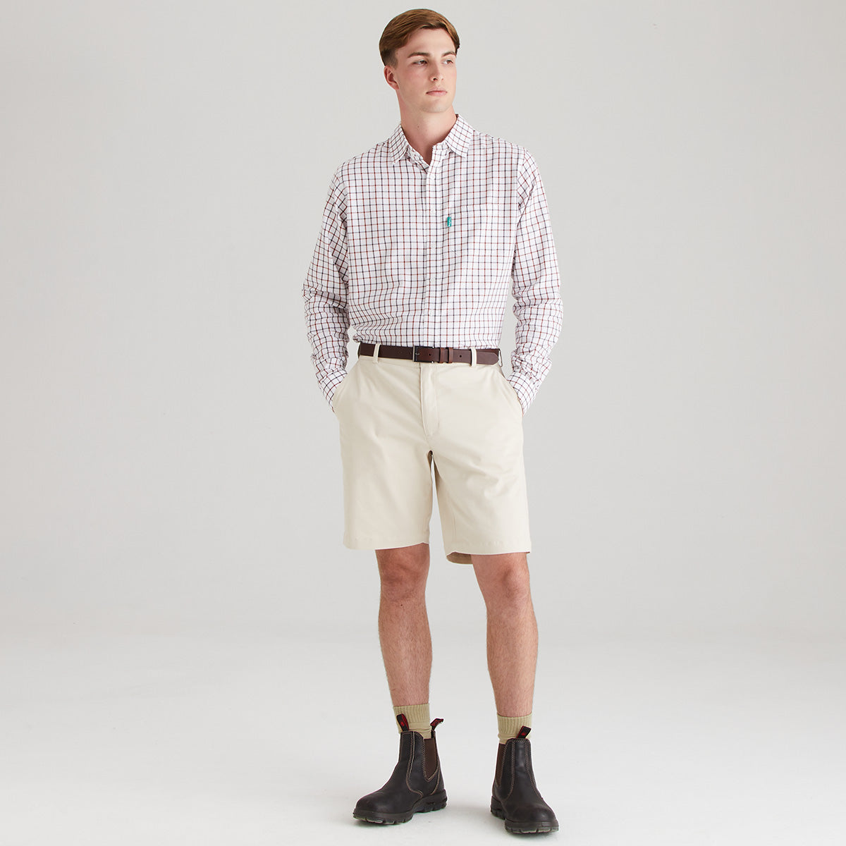 Man wearing a checkered shirt, beige shorts, and dark boots on a light gray background