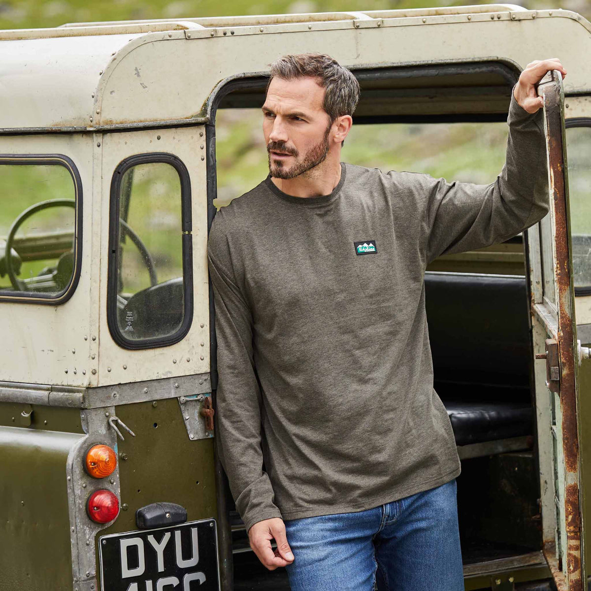 Man standing next to a vintage vehicle wearing a light bark marl long-sleeve shirt with a logo.