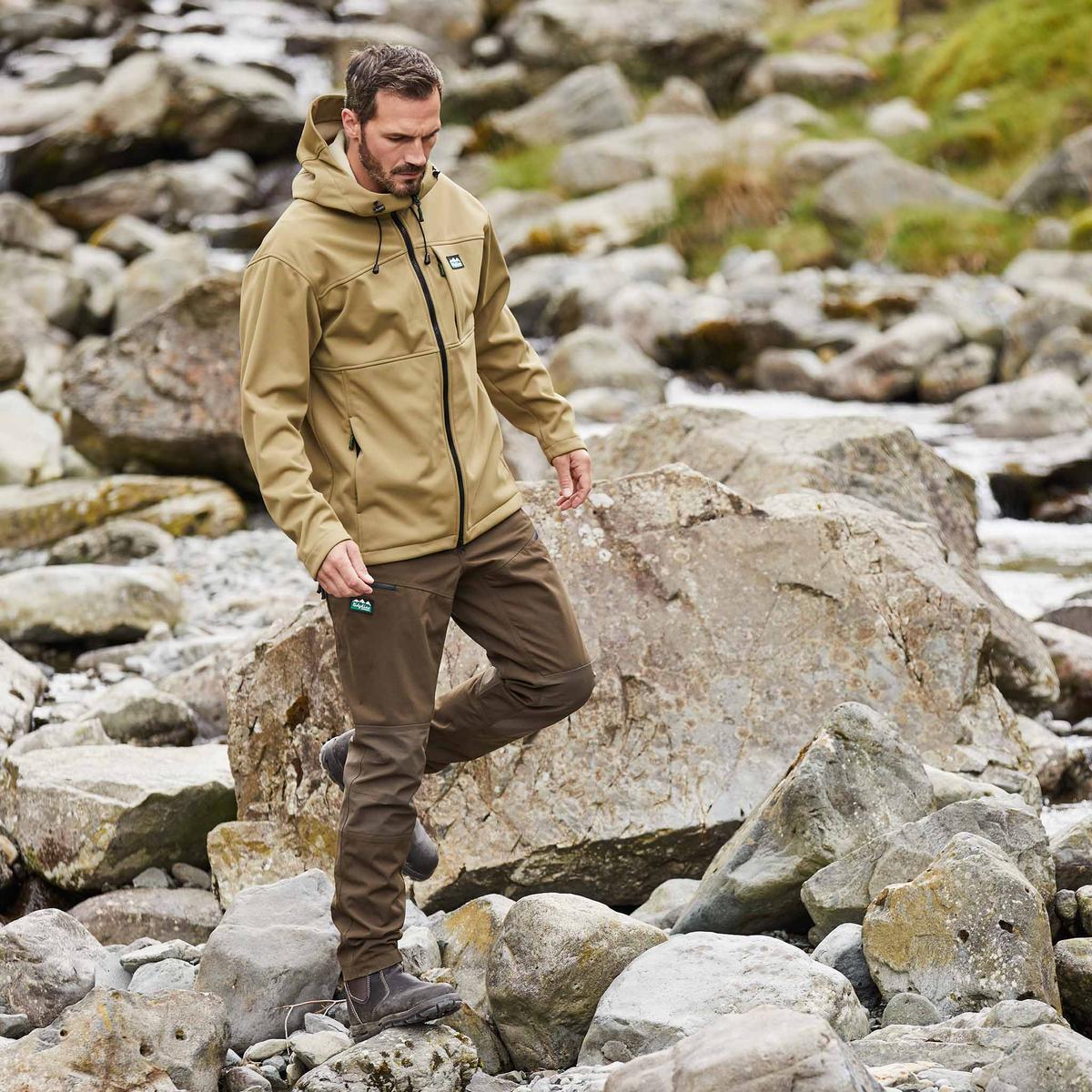Man wearing a brown gradient jacket with a hood, walking across rocks