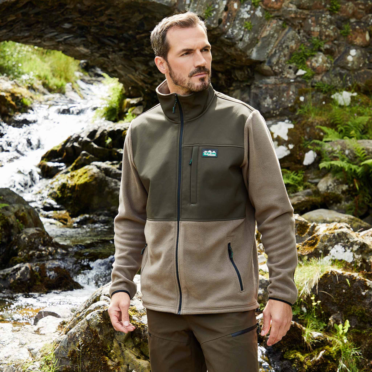 Man wearing Two-tone black and green Windproof fleece jacket with a Ridgeline Clothing logo In a outdoor setting standing next to a stream