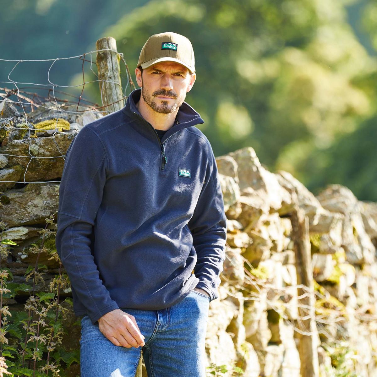 Man wearing a Navy fleece pullover with a quarter zipper and a Ridgeline clothing logo on the chest. & wearing a hat with Ridgeline clothing logo in centre