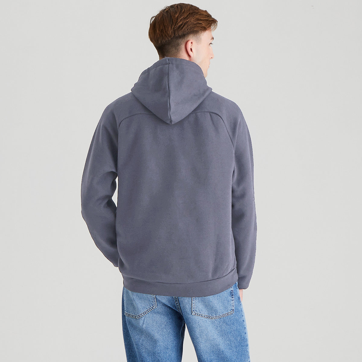 Person wearing a gray hoodie and blue jeans on a light gray background