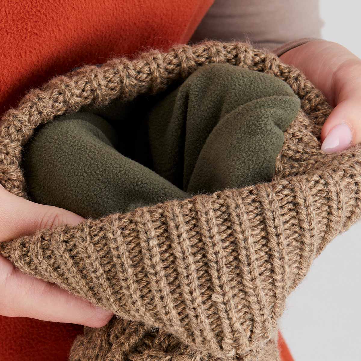 Brown knitted fabric with green fabric inside, held by hands against a neutral background