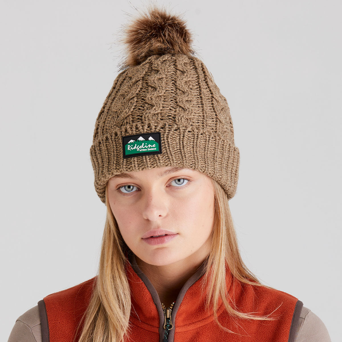 woman wearing a brown knit beanie with a ridgeline clothing logo on a light grey background