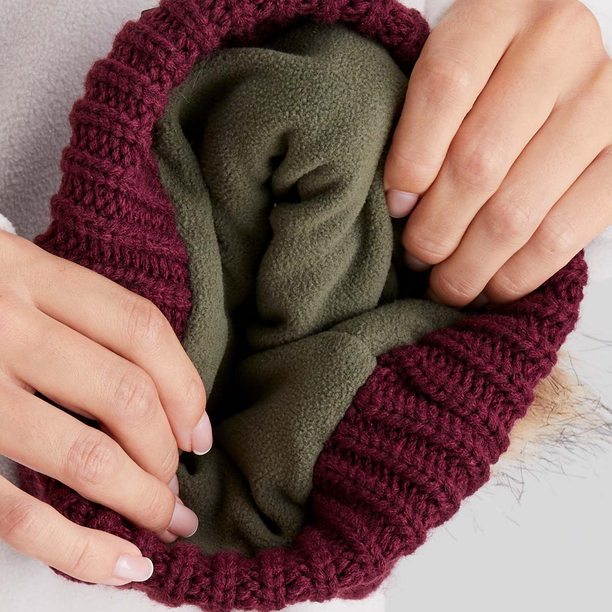 Close-up of hands holding a green fabric item with a maroon knitted cover.