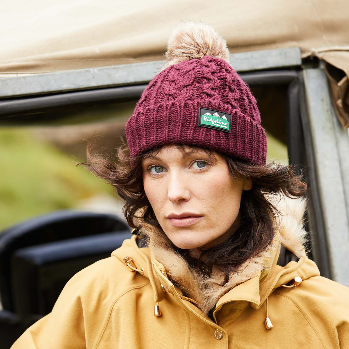 Woman wearing a red Nordic Fleck bobble hat Standing next to a jeep