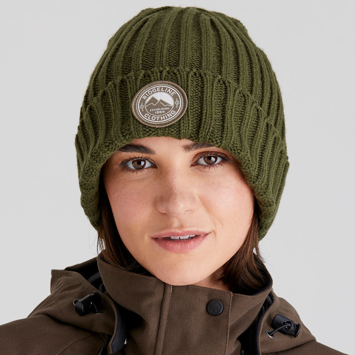Person wearing a green knit beanie with a logo on a grey background