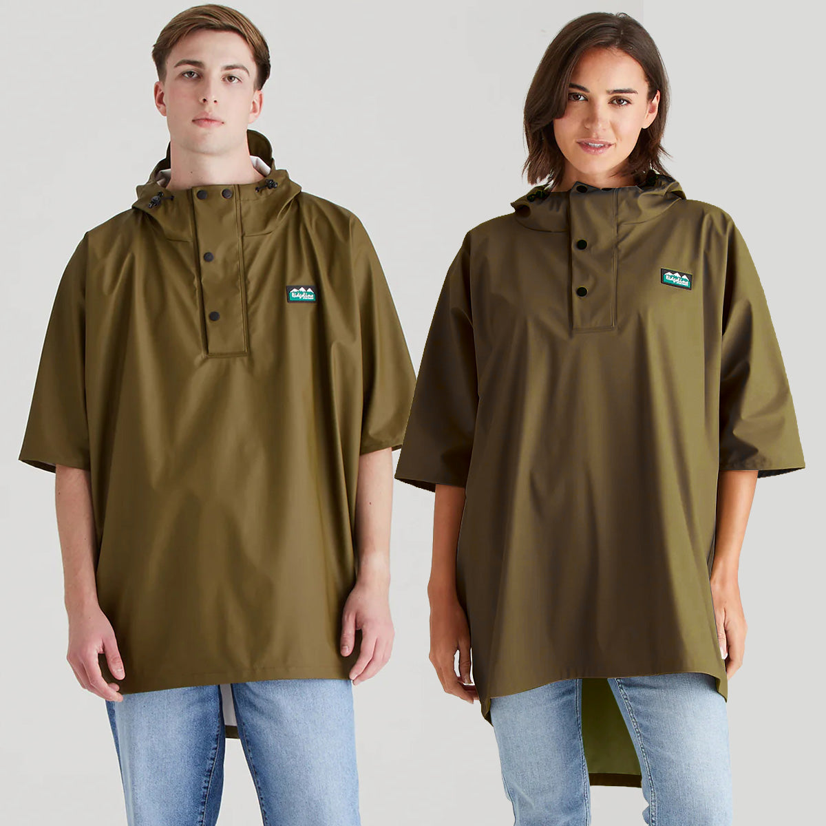 A man and a woman modeling matching olive green ponchos short-sleeve rain ponchos with a buttoned placket and a small chest logo patch, shown against a light gray studio background.