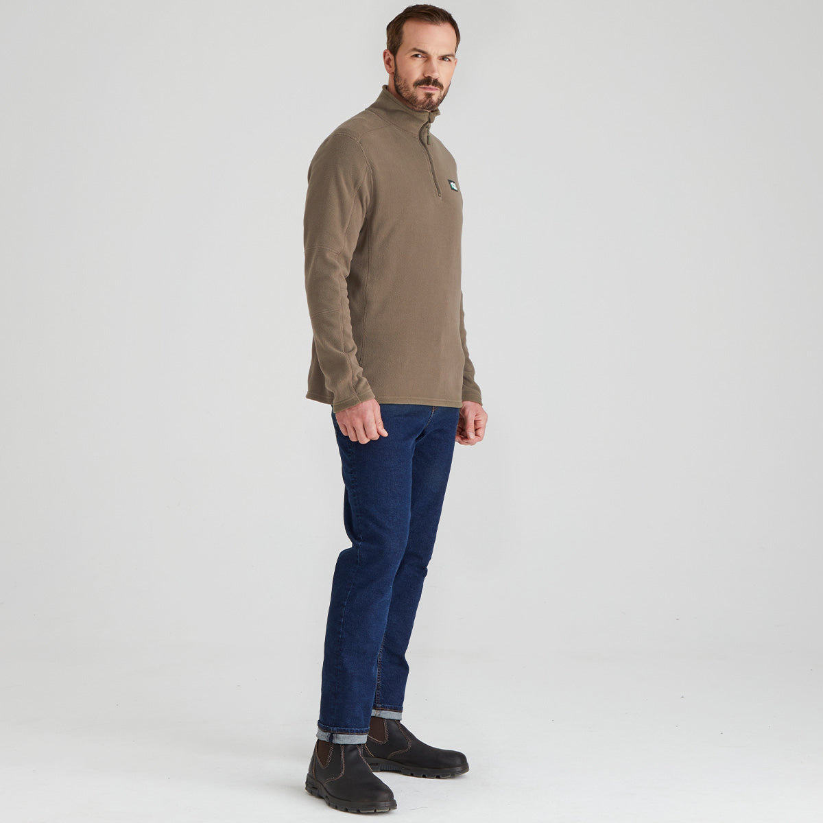 Man wearing a brown fleece jumper and blue jeans on a white background