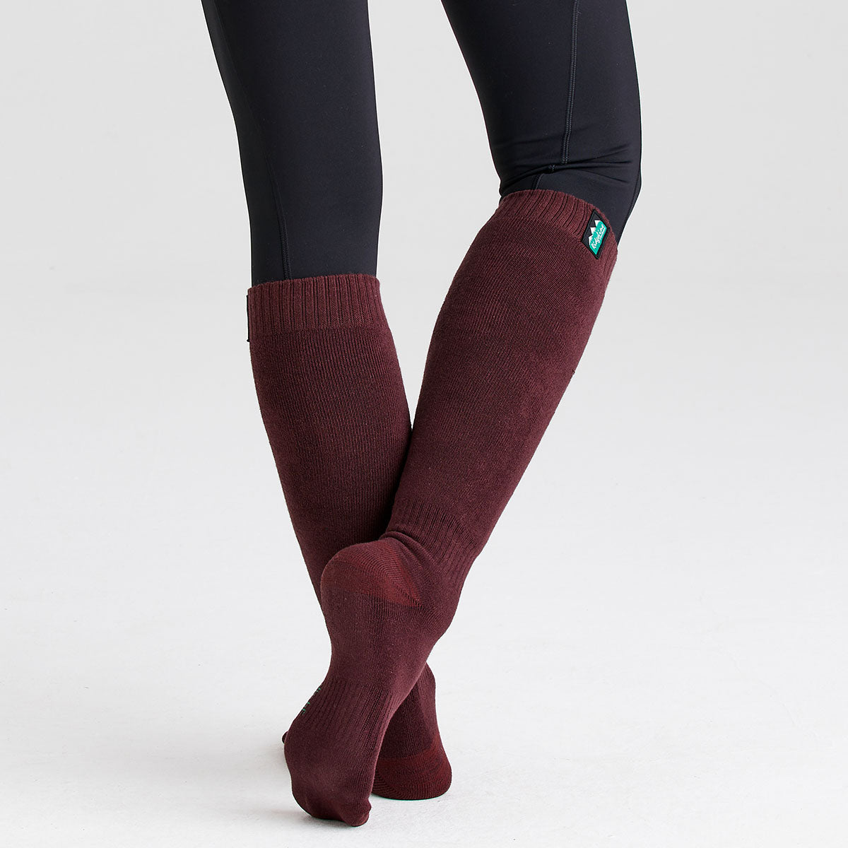 Burgundy knee-high cotton work socks worn with crossed legs, featuring a ribbed knit design and full-length coverage for warmth and comfort.