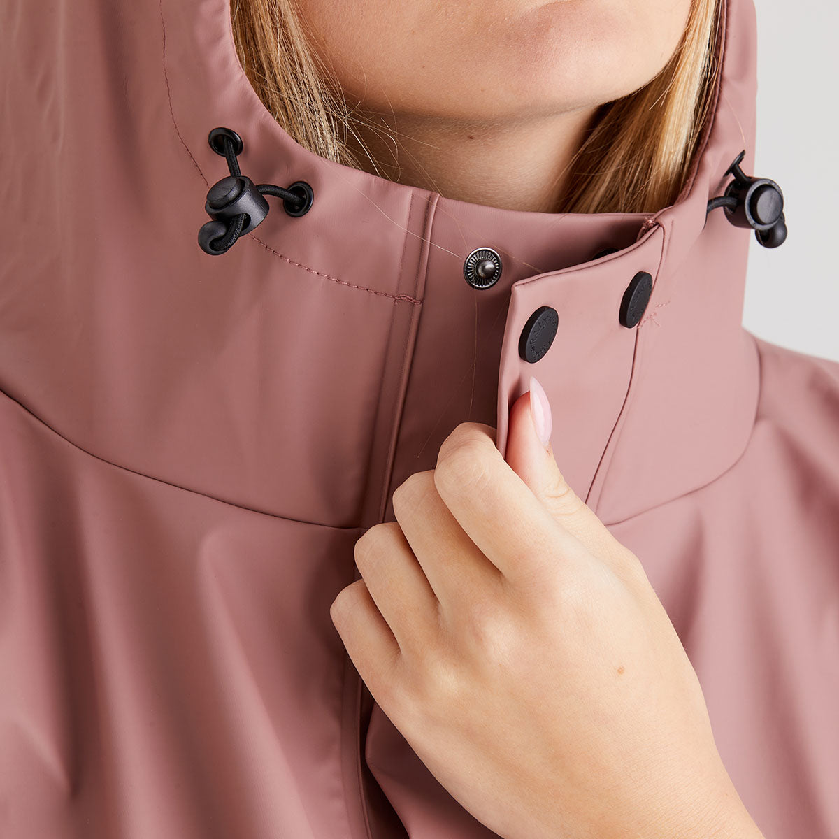 Close-up of a person wearing a pink raincoat with a hood, focusing on the jacket's texture and design.