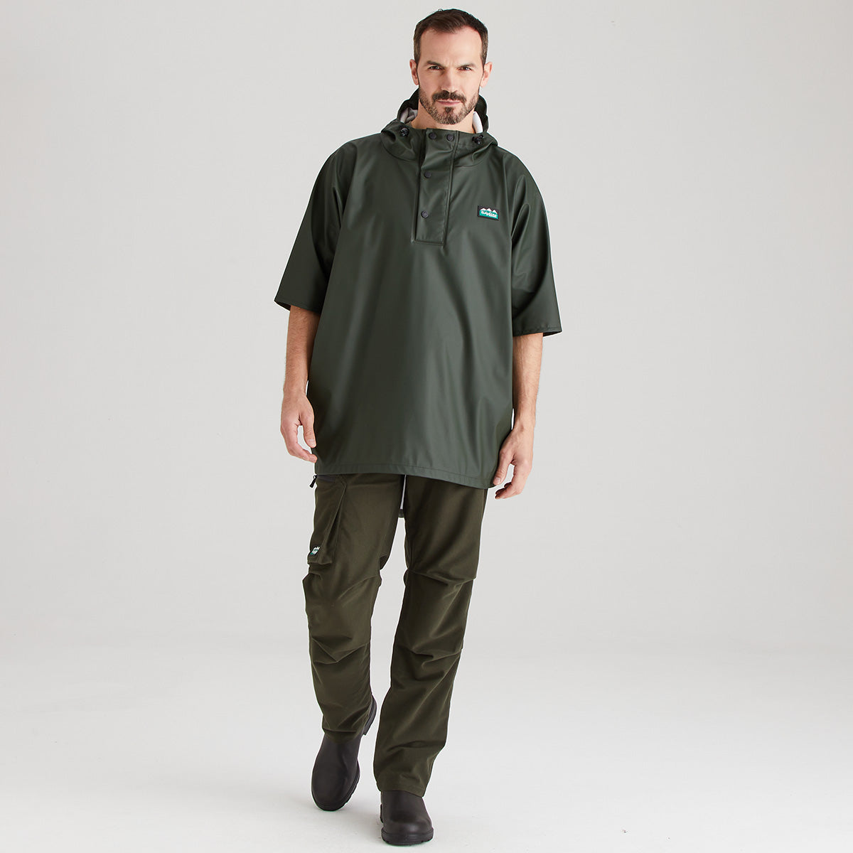Man wearing a green raincoat and pants on a light gray background