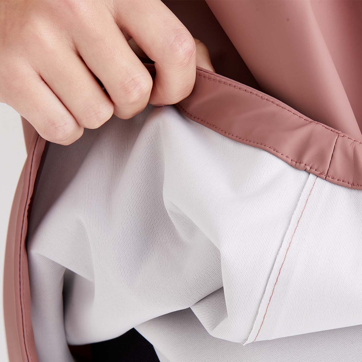 Close-up of a hand adjusting the collar of a light gray jacket with a pink inner lining.