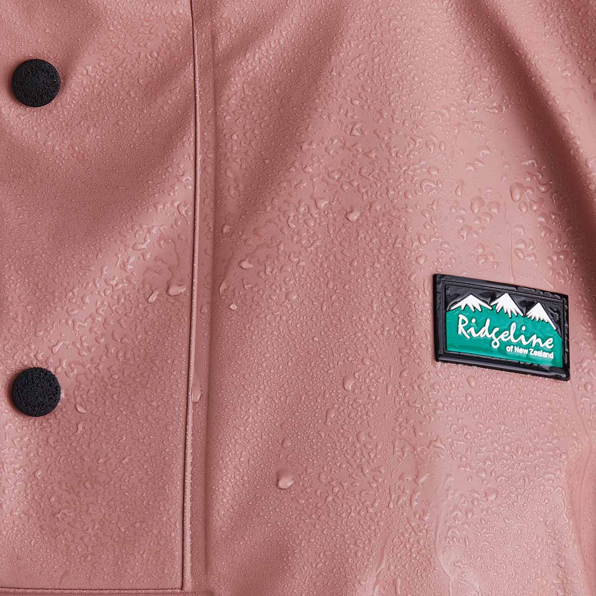 Pink raincoat with water droplets and a visible brand logo on a close-up view.