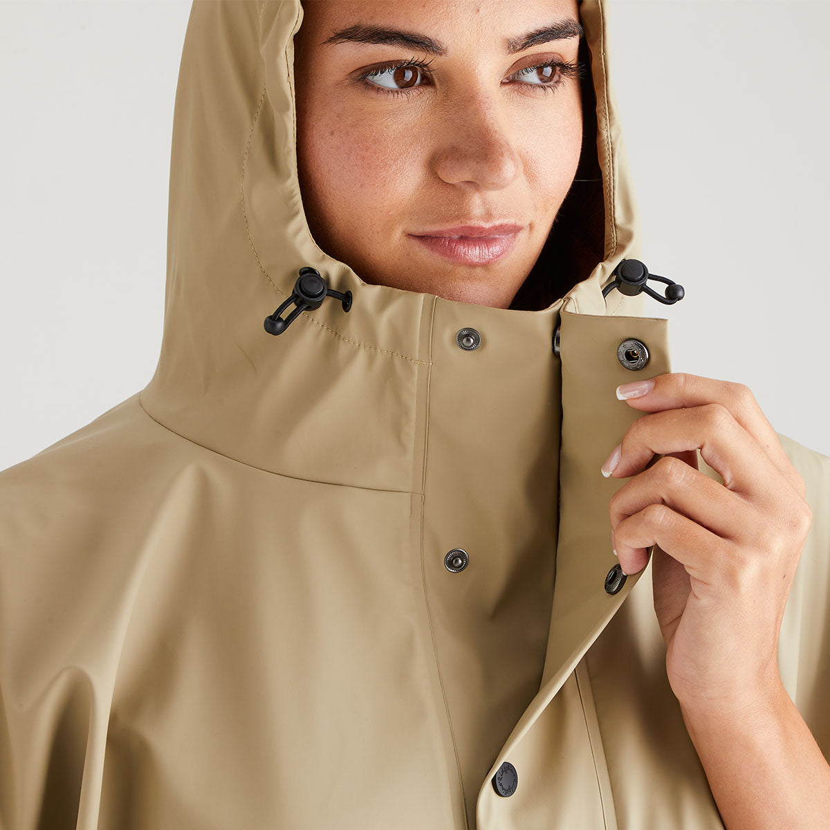 Person wearing a beige raincoat with a hood against a light background