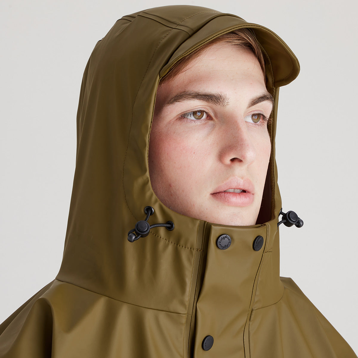 Person wearing a brown raincoat with a hood on a plain background