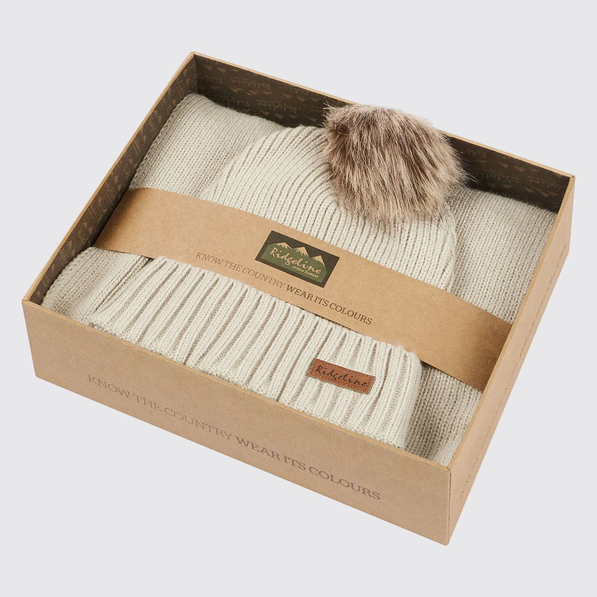 Cream ribbed knit beanie hat with faux fur pom pom in branded gift box, angled view.