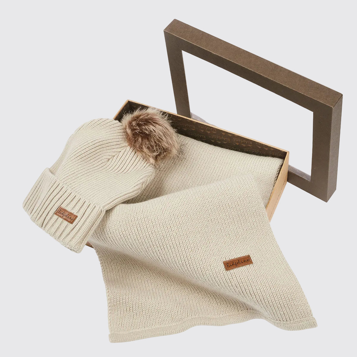 Cream ribbed knit beanie hat with faux fur pom pom and matching scarf in open gift box, angled view