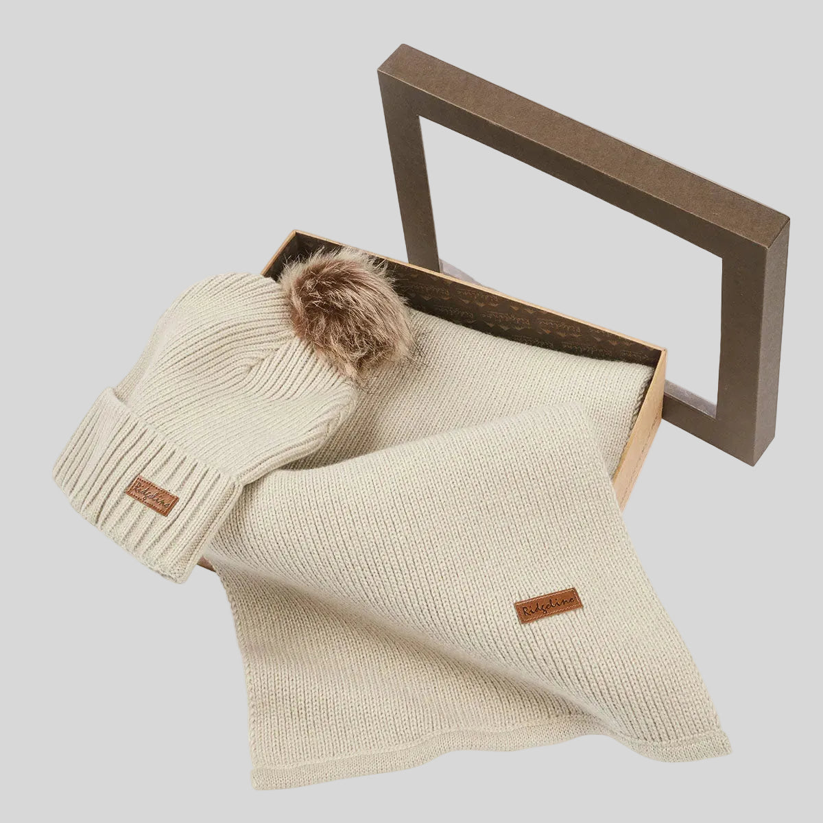 Cream ribbed knit beanie hat with faux fur pom pom and matching scarf in open gift box, angled view